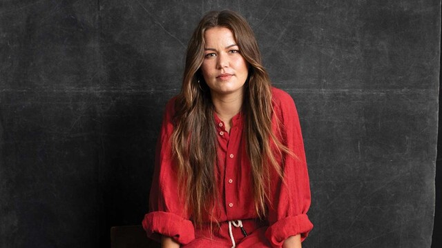 Portrait of Vanessa Turnbull-Roberts in red dress sitting down against black background