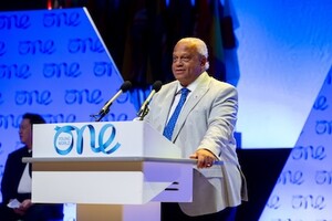 Lord Dr Michael Hastings CBE addressing the audience at the podium on the presentation stage of a OYW summit