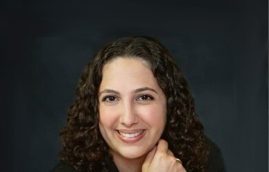 Ariane portrait, wearing black blazer against dark grey black background